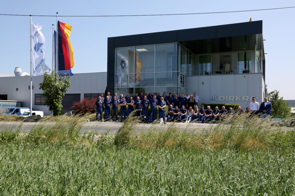 Das Foto zeigt ein Gebäude der DIRKRA Group, vor dem die Mitarbeitenden sich gemeinsam aufgestellt haben.